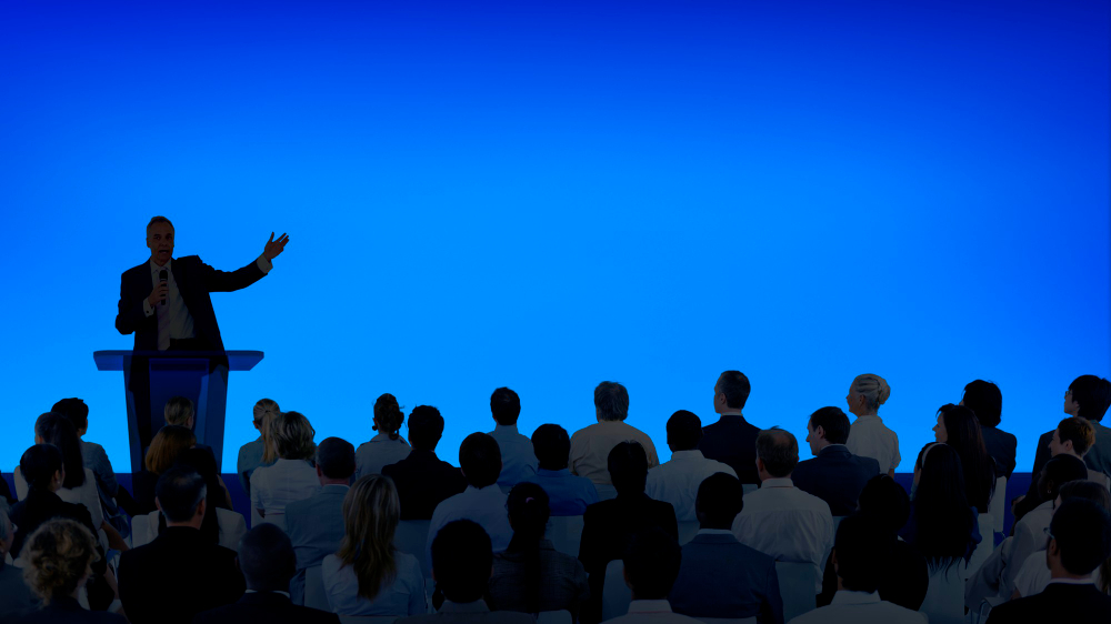 Dicas de como fazer uma palestra na sua empresa | Homem palestrando para muitas pessoas em auditório azul | Smartalk